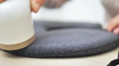 Kadın, modern el yapımı elektrikli kumaş traş makinesi kullanarak kazaktan hap çıkarıyor. Kıyafet bakım konsepti