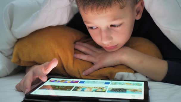 Menino Brinca Tablet Enquanto Deitado Sob Cobertor Assistindo Desenhos Animados — Vídeo de Stock