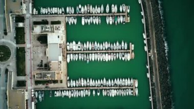 Alacakaranlıkta, turkuaz okyanus su marinasında park etmiş lüks yatların üstündeki tepeden aşağı hava manzarası..