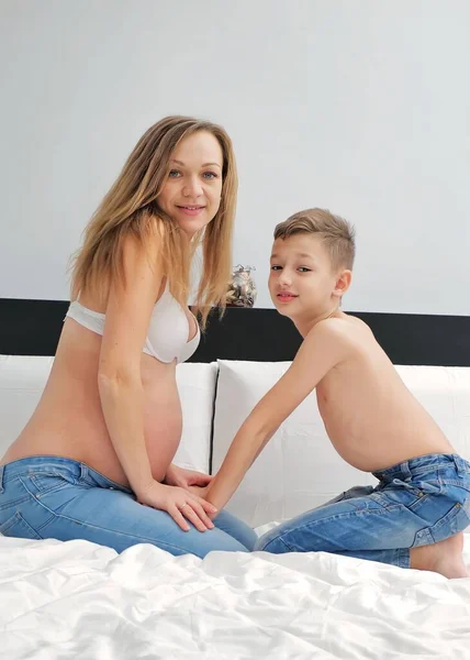 Pregnant mom talking and playing with her child in the bedroom. Mother with son sharing good emotions while relaxing at home