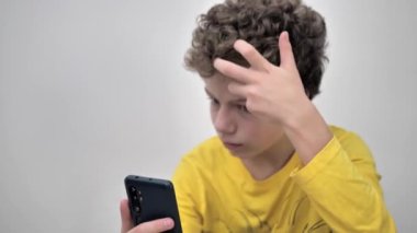 Close-up of teenage boy squeezing pimples while looking at phone.