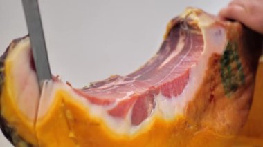 Macro shot of man cutting the Italian or Iberian traditional ham with a sharp cut. Close up on hands and the blade.