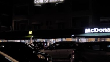 Rome, Italy, December 31. 2022. night shot of the exterior of a modern McDonalds. Visitors to the restaurant come in and out. cars pull up for their portion of fast food.