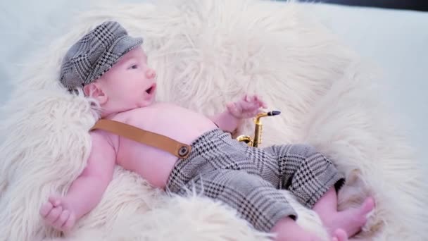 赤ちゃんは白い毛皮の上に帽子とおもちゃのサクソフォンをかぶっています — ストック動画