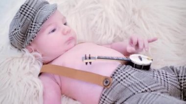 a newborn baby is lying on a white fur in a cap and with a guitar.