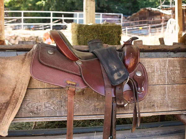 The saddle is brown on the fence in a shallow depth of field. leather saddle, harness for horses. Western saddles for horses on the rack, ready for dressage training. Equestrian sport background.