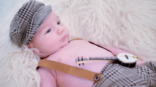 新生児は白い毛皮の上に帽子とギターをかぶっています — ストック動画