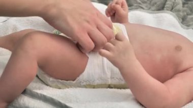 baby care, a woman changes the diapers of a baby lying on a bed.