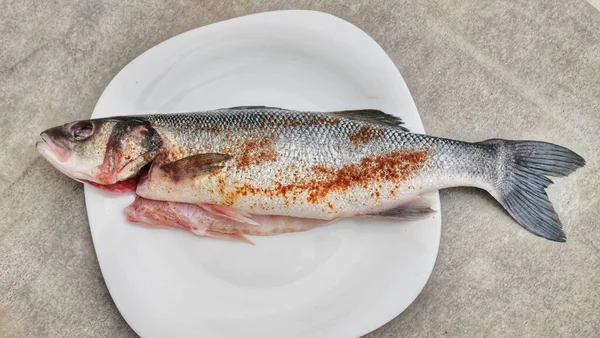 One fresh fish on a white plate, salt and spices on a white plate. Salting and marinating fish, restaurant, cookbook, culinary blog, advertising. High viewing angle