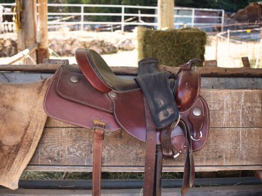 The saddle is brown on the fence in a shallow depth of field. leather saddle, harness for horses. Western saddles for horses on the rack, ready for dressage training. Equestrian sport background. clipart