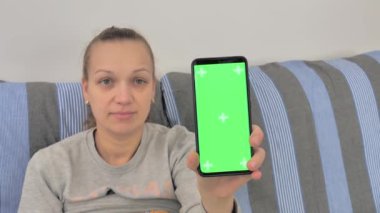 Portrait of a girl holding a smartphone in front of her, showing a green screen mobile phone to the camera, advertising an app service website, advertising a digital device