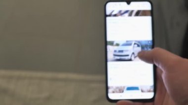 Bir adam şantiyeden araba almayı seçiyor. Akıllı telefon uygulaması almak için kullanılmış araca bakıyorum. Yakın çekim. Ekran bulanık. 4K UHD