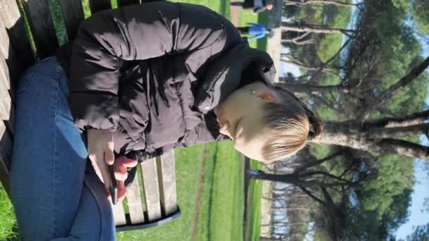 垂直屏风 阳光明媚的日子里 穿着黑色夹克 穿着蓝色牛仔裤 拿着手机的年轻女子 — 图库视频影像