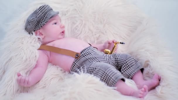 赤ちゃんは白い毛皮の上に帽子とおもちゃのサクソフォンをかぶっています — ストック動画