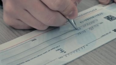 Close-up image of a persons hand filling out a bank check for 1000 euros