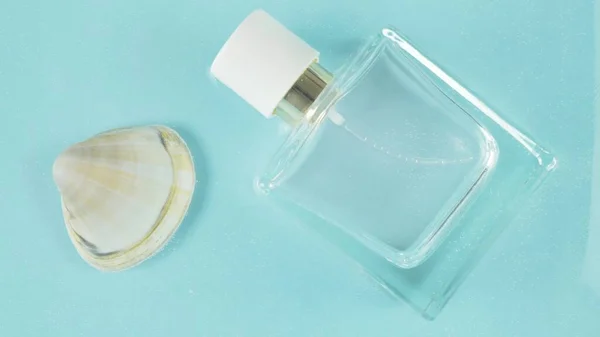 Glass perfume bottle and sea shells in spray water background. Marine summer fragrance concept.