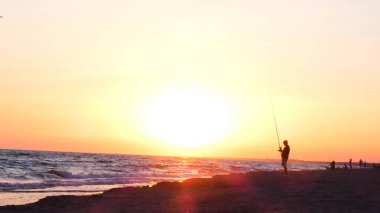 Mutlu balıkçı doğa siluetinde deniz kenarında balık yakalıyor..