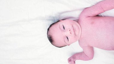 Kıllı, esmer, tatlı, yeni doğmuş bebek beyaz çarşafın üzerinde yatıyor. Çıplak ay bebeği, yarı vücut çekimi, mesaj için kopyalama alanı. Yüksek açı, üst görünüm