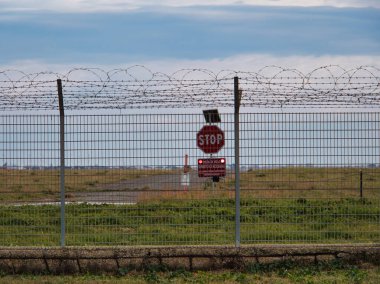 Havaalanı güvenlik çit sistemi, dikenli telle çevrili, güvenlik yasaklı bölge dur levhası ve arkada uçaklar var..