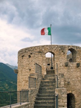 Dağın arka planında İtalyan bayrağı olan eski kalenin kulesi..