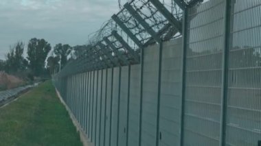 Mavi gökyüzünün altında dikenli telleri olan beton çitler.