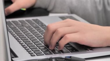 Ofis masasında dizüstü bilgisayarda yazı yazan bir gencin yakın çekimi. Kapalı alanda bilgisayarla çalışan tanınmayan bir genç. kırpılmış kenar görünümü.