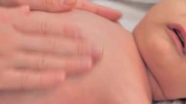 Genç, şefkatli anne, yeni doğmuş oğluna masaj yapıyor. Küçük çocuk büyük beyaz yatakta yüzüstü yatıyor. Bebek sağlığı hizmetleri için alıştırmalar