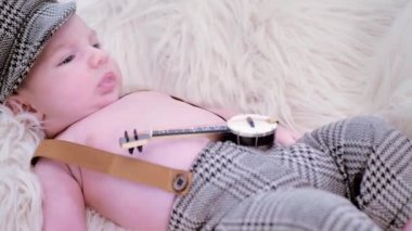 a newborn baby is lying on a white fur in a cap and with a guitar.