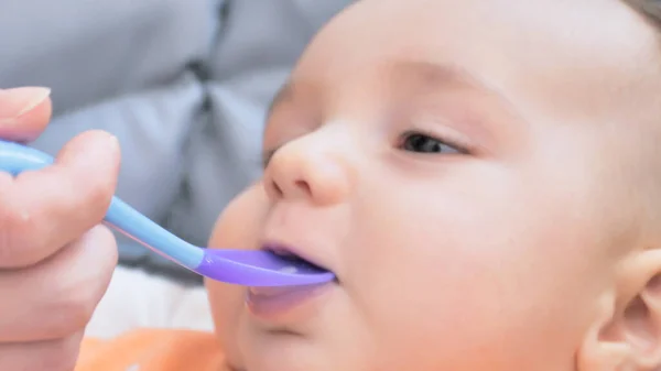 stock image Mother hand feeding baby with spoon, boy sitting eating food on chair at home. Happy family. Smiling happy child