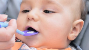 Anne bebeği kaşıkla besliyor, çocuk evde sandalyeye oturup yemek yiyor. Mutlu bir aile. Gülümseyen mutlu çocuk