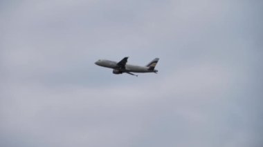 Long shot, passenger plane approaching to land. Airliner flies in cloudy gray sky, rain.