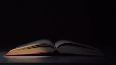 Karanlık bir stüdyoda masanın üzerinde açık bir kitap. Projektörden bir ışık demeti sayfalarını aydınlatır ve üzerlerindeki toz bulutu uçar. Yavaş çekim, yakından.
