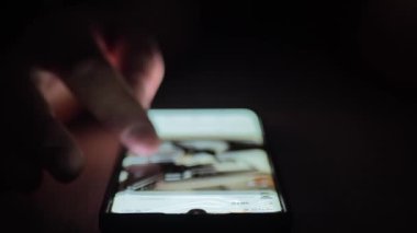 Karanlık bir odada cep telefonu kullanmak. İnsan elleri arabaların fotoğraflarını tarıyor. Moda sosyal medya.