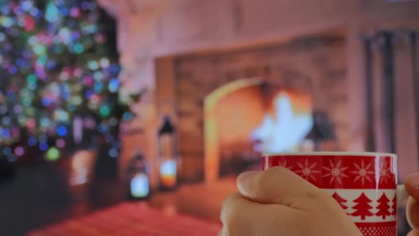 ホットミルク コーヒーの赤いマグカップをバックグラウンドで閉じます 暖炉が燃えている映画的な休日のバックグラウンド 家族の集まり お祝い 愛とケアのコンセプト — ストック動画