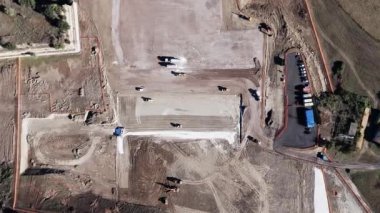 İnşaat alanında ekipmanlar çalışıyor: bir yol silindiri ve bir buldozer inşaat için kum tabanını hazırlıyorlar. Üst görüntü insansız hava aracı görüntüsü