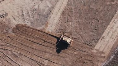 Toprak hareket eden buldozerin havadan görünüşü. Takip edilen bir buldozer kum ocağında çalışıyor. Toprak hareket eden buldozerin sanayi bölgesinde kum çıkarışının en üst görüntüsü.