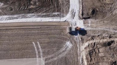Buldozerli inşaat. Yukarıdan bak. Sarı bir buldozer elinde kovayla yere düşüyor. İnsansız hava aracı görüntüleri. Dünya inşa çalışmaları