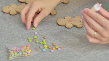 Kadın eli zencefilli adam şeklinde Noel pastasını beyaz krema ve renkli karamel ile süslüyor. yakın plan