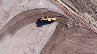 Toprak hareket eden buldozerin havadan görünüşü. Takip edilen bir buldozer kum ocağında çalışıyor. Toprak hareket eden buldozerin sanayi bölgesinde kum çıkarışının en üst görüntüsü.