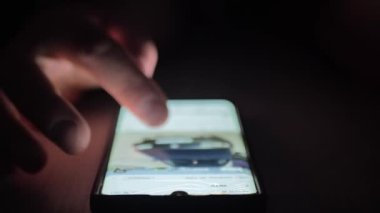 Karanlık bir odada cep telefonu kullanmak. İnsan elleri arabaların fotoğraflarını tarıyor. Moda sosyal medya.