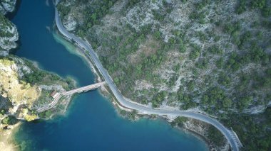 Hava manzarası, gür yeşil ve kayalık arazilerle çevrili engebeli dağların arasından kıvrılarak geçen dolambaçlı bir yol gösteriyor. Yol kıvrılır ve döner. Manzarada zorlu bir sürüş sunar.
