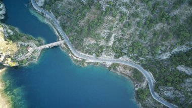 Hava perspektifi, yüksek dağların arasına yerleşmiş bir göl gösteriyor, çarpıcı bir doğal manzara yaratıyor. Gölün sakin suları onu çevreleyen engebeli tepeleri ve yemyeşil alanları yansıtır.