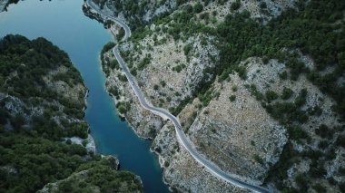 Hava perspektifi, yüksek dağların arasına yerleşmiş bir göl gösteriyor, çarpıcı bir doğal manzara yaratıyor. Gölün sakin suları onu çevreleyen engebeli tepeleri ve yemyeşil alanları yansıtır.