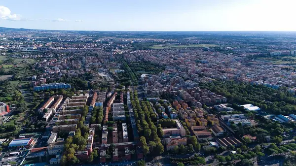 The aerial view showcases a cityscape filled with an abundance of lush green trees, providing a refreshing sight amidst the urban environment. The trees are scattered throughout the city, lining