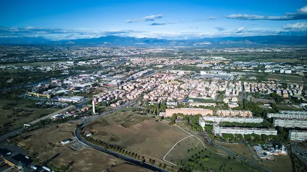 The aerial view showcases a cityscape filled with an abundance of lush green trees, providing a refreshing sight amidst the urban environment. The trees are scattered throughout the city, lining