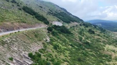 Sakin bir yol, yoğun yeşillikler ve sislerle kaplı tepelerle çevrili yeşil bir dağ yamacından geçiyor. Güneş bulutların arasından geçmek için çırpınıyor, yemyeşil bir ışık salıyor.