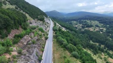 Dolambaçlı yol bulutlu bir gökyüzünün altındaki yeşil tepelerle çevrili sakin manzarayı zarifçe dolaşır. Bu huzurlu ortam doğanın özünü yakalıyor güzellik, maceraperestleri davet ediyor