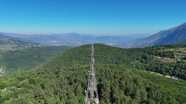 Canlı yeşil tepelerin üzerinde yükselen bir iletişim kulesi, uçsuz bucaksız vadilere ve uzak dağlara karşı dimdik ayakta duruyor. Açık mavi gökyüzü manzaranın dingin güzelliğini arttırır.