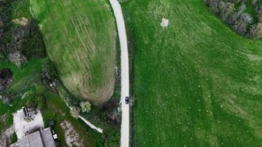 Kıvrımlı bir yol canlı yeşil tarlaları kesiyor, doğanın güzelliğini tüm ihtişamıyla gösteriyor. Yalnız bir araç yol boyunca seyahat eder. Geniş alanların arasında macera hissi yaratır.