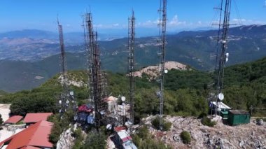 Yüksek iletişim kuleleri zirveye hakim, yemyeşil ve parlak gökyüzünün altındaki uzak dağlarla çevrili..